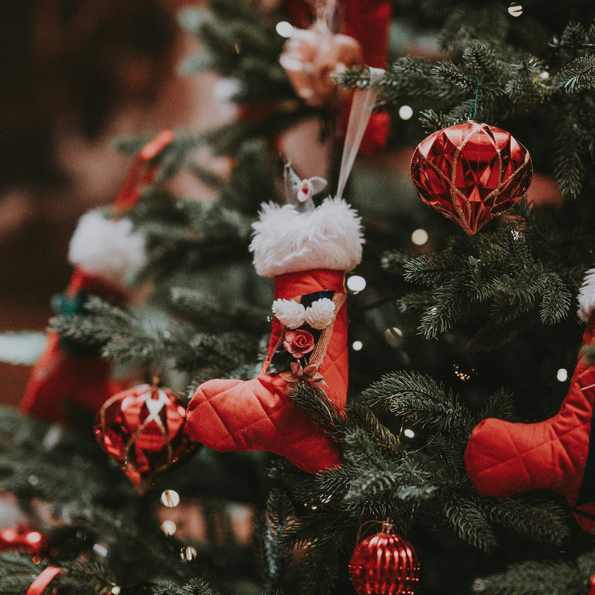 Decorative red stocking hanging on a Christmas tree with red ornaments.